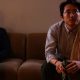 Steven Yeun como Richard sentado no sofá tomando uma cerveja em imagem do filme The Humans.