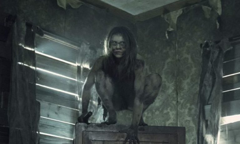 Mulher selvagem segurando algo em cima de alguma coisa em casa abandonada no episódio 6 da 11ª temporada de The Walking Dead.