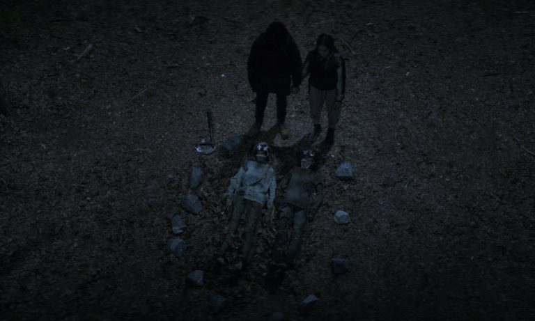 Elton e Asha de mãos dadas e fazendo uma oração sob 2 zumbis no chão com flores em seus olhos no episódio 6 da 2ª temporada de The Walking Dead: World Beyond.