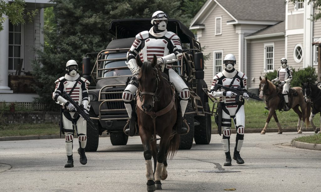 Dois soldados de Commonwealth a cavalo e dois andando em Alexandria no episódio 12 da 11ª temporada de The Walking Dead.