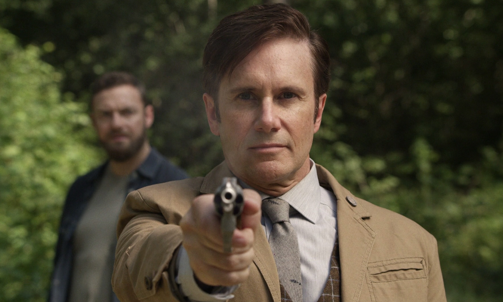 Lance apontando sua arma com Aaron ao fundo em cena do episódio 12 da 11ª temporada de The Walking Dead.