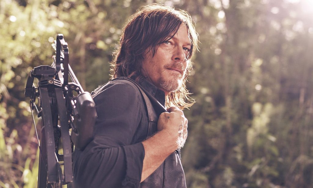 Norman Reedus como Daryl Dixon segurando sua besta nas costas em imagem promocional de The Walking Dead.