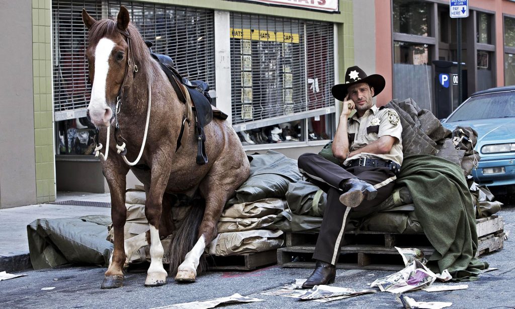 Rick Grimes sentado ao lado de seu cavalo durante os bastidores do primeiro episódio de The Walking Dead.