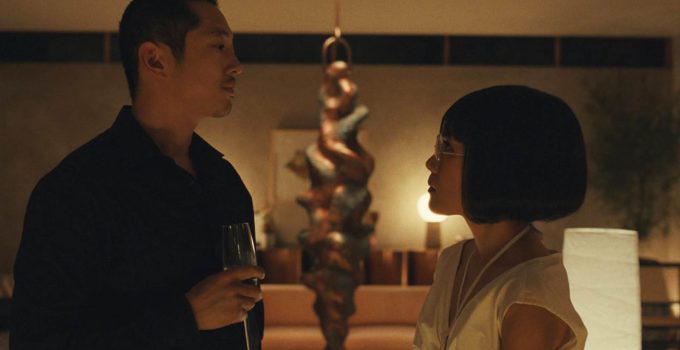 Steven Yeun como Danny Cho segurando uma taça e encarando Ali Wong como Amy Lau em cena da série Beef, da Netflix.