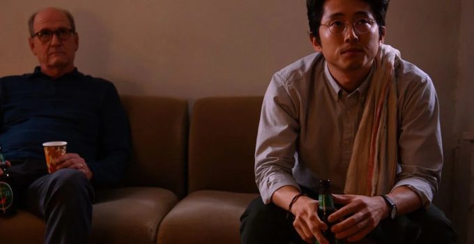 Steven Yeun como Richard sentado no sofá tomando uma cerveja em imagem do filme The Humans.