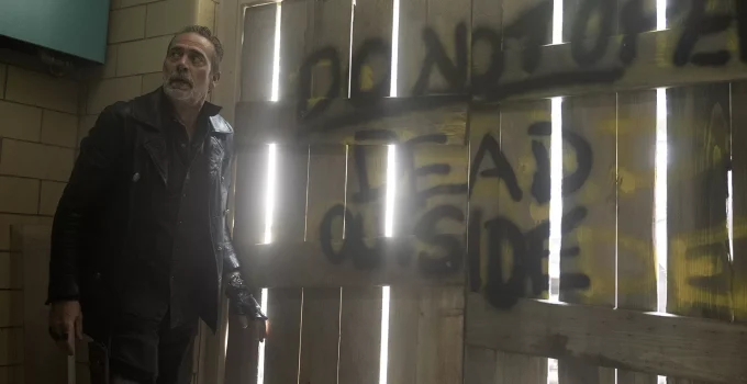 Negan olhando para algo ou alguém com uma porta ao fundo com a frase "Não abra, mortos do lado de fora" em cena do episódio 5 da 1ª temporada de The Walking Dead: Dead City.