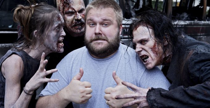 Robert Kirkman fazendo joinha ao lado de 3 zumbis da 1ª temporada de The Walking Dead.