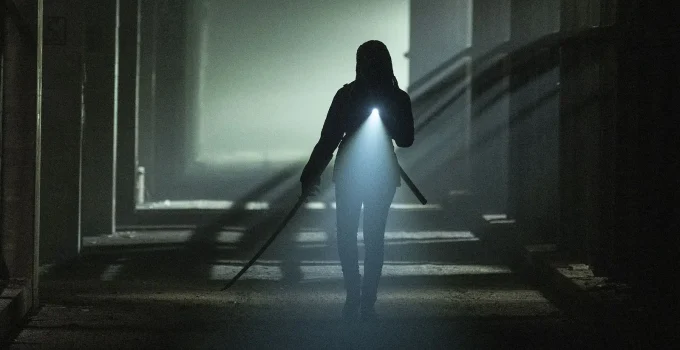 Michonne com sua katana e utilizando uma lanterna em um local desconhecido e escuro em cena do Episódio 3 de The Walking Dead: The Ones Who Live.